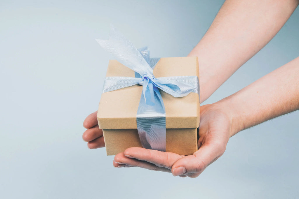 Person holding a small gift box with a blue ribbon against a light gray background